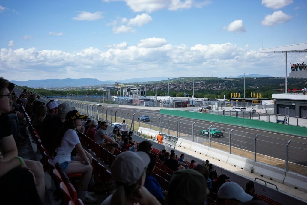 Archival photograph of spectators in a grandstand watching race cars on a circuit under a blue sky; not the 2026 United States Grand Prix qualifying session.