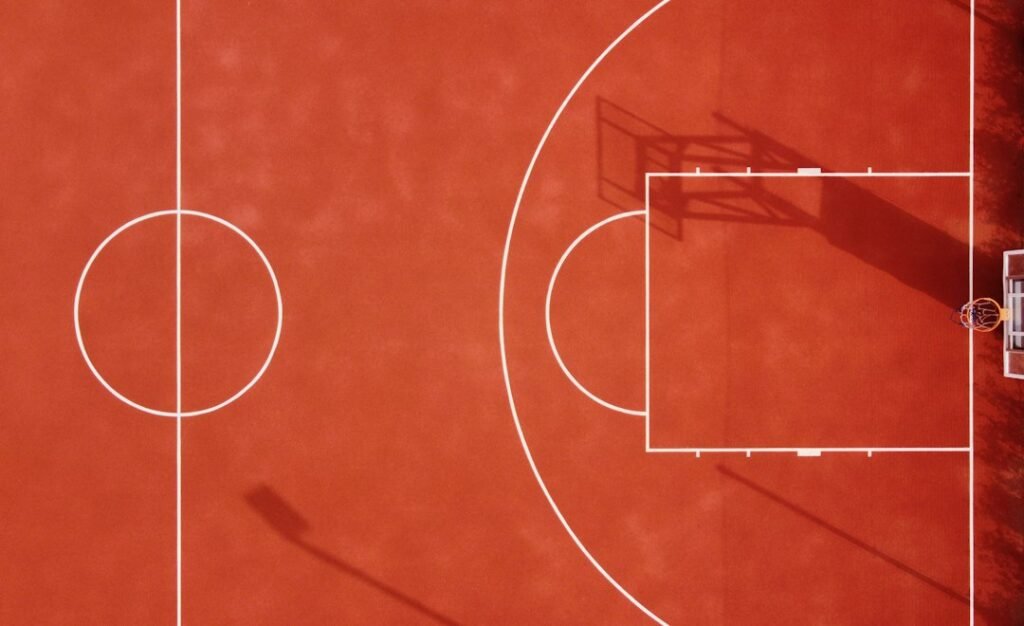 Overhead view of a red basketball court with white lines and shadows; illustrative stock photo, not footage from Mavericks versus Thunder; Oleksii S / Unsplash