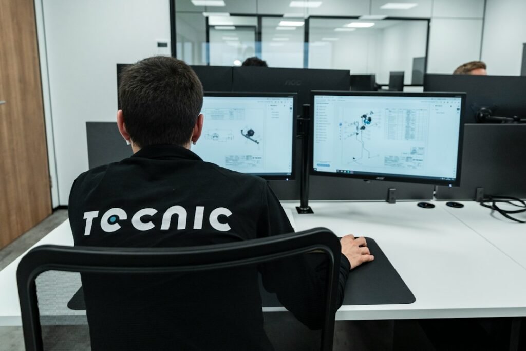 Illustrative industrial engineering workstation with dual monitors displaying technical drawings; not a Dassault Systèmes office or event